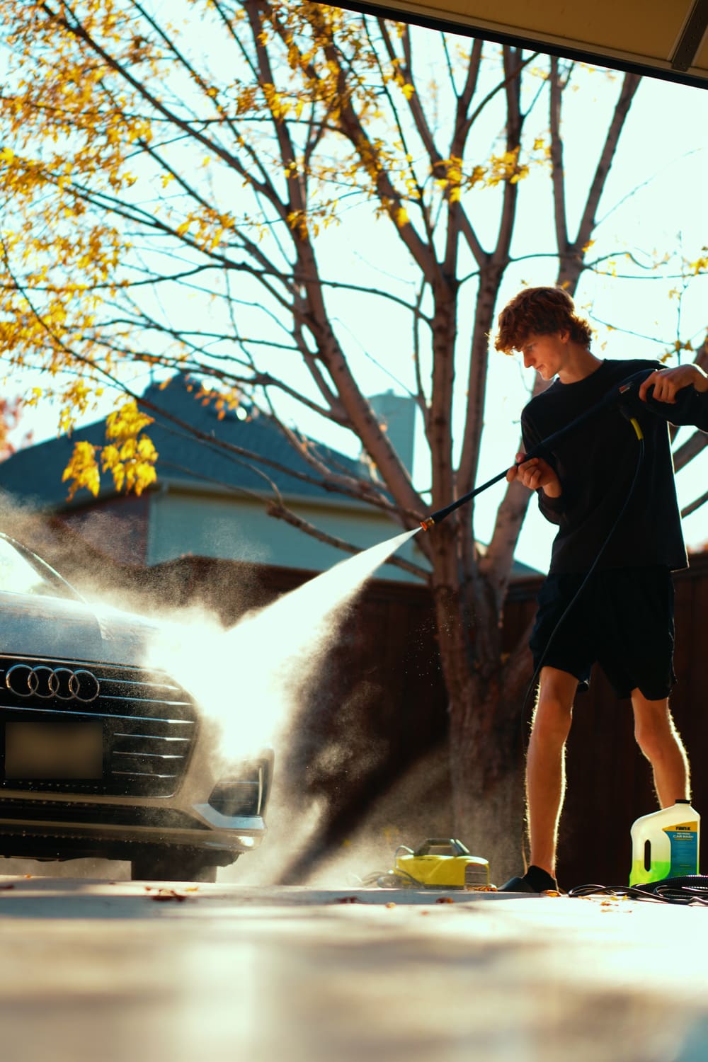 Pressure washing a car in a sunny driveway on an autumn afternoon, with the spray catching the light.
